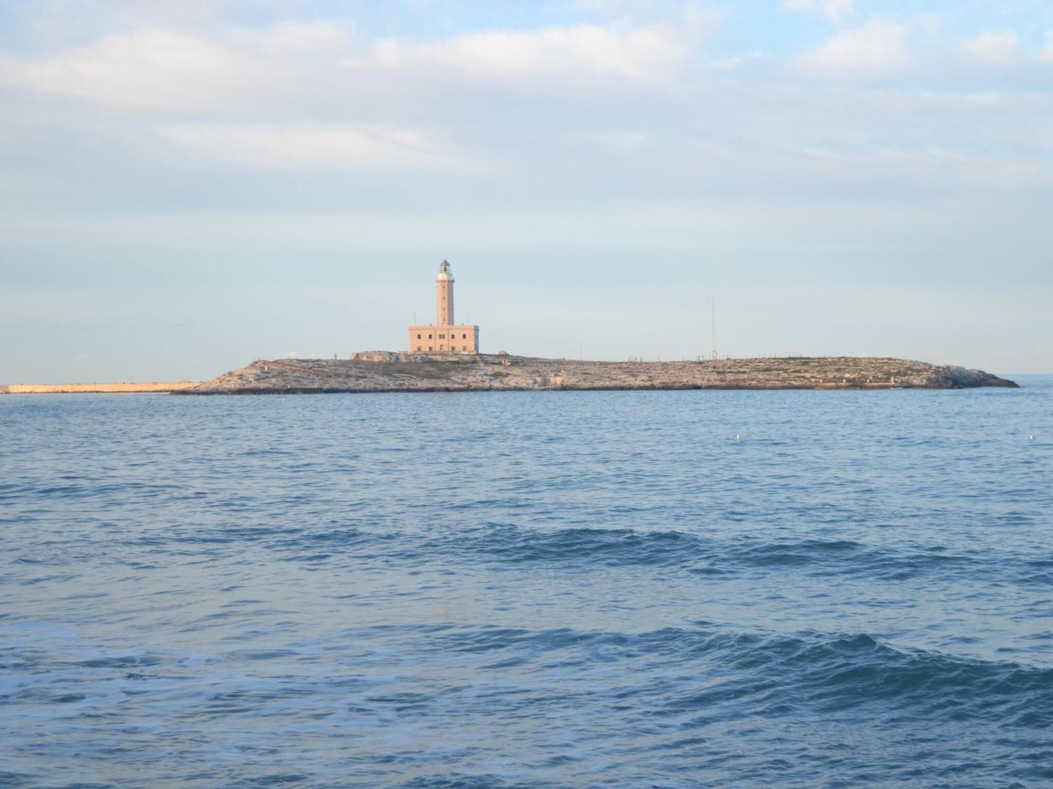 Un faro su un'isola rocciosa, con un mare calmo in primo piano.