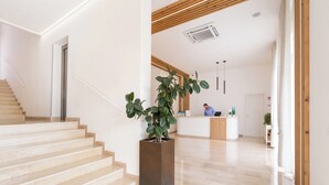 Un hall d’hôtel moderne avec un escalier, un comptoir d’accueil et une grande plante en pot.