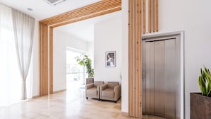 Un hall d’entrée spacieux avec un plafond à lambris en bois, un comptoir de réception, deux canapés, une grande plante en pot et une porte.