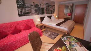 Een hotelkamer met een stadsmuur, een rode bloemenbank, een bed met witte lakens, een houten nachtkastje en een tijdschrift op de tafel.