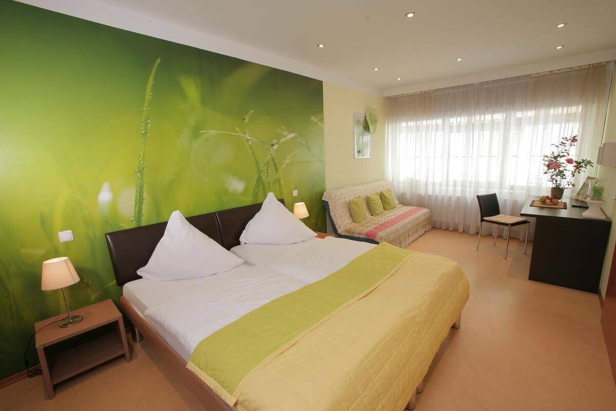 A hotel room with a bed, a desk, a chair, and a green wall.