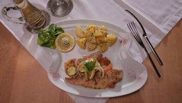 Un plato con un filete de pescado, rodajas de limón, patatas y una ensalada acompañante sobre un mantel blanco.