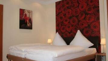 Una cama doble con sábanas blancas, dos mesitas de noche con lámparas y un papel tapiz floral rojo en la pared.