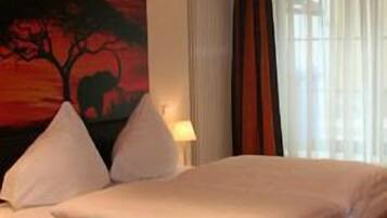 Un dormitorio con una cama, una mesita de noche, una lámpara y un cuadro grande de un árbol en la pared.