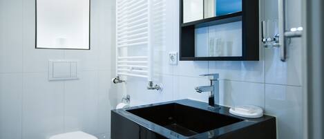 A modern bathroom with a black sink, white toilet, and a mirror above the sink.