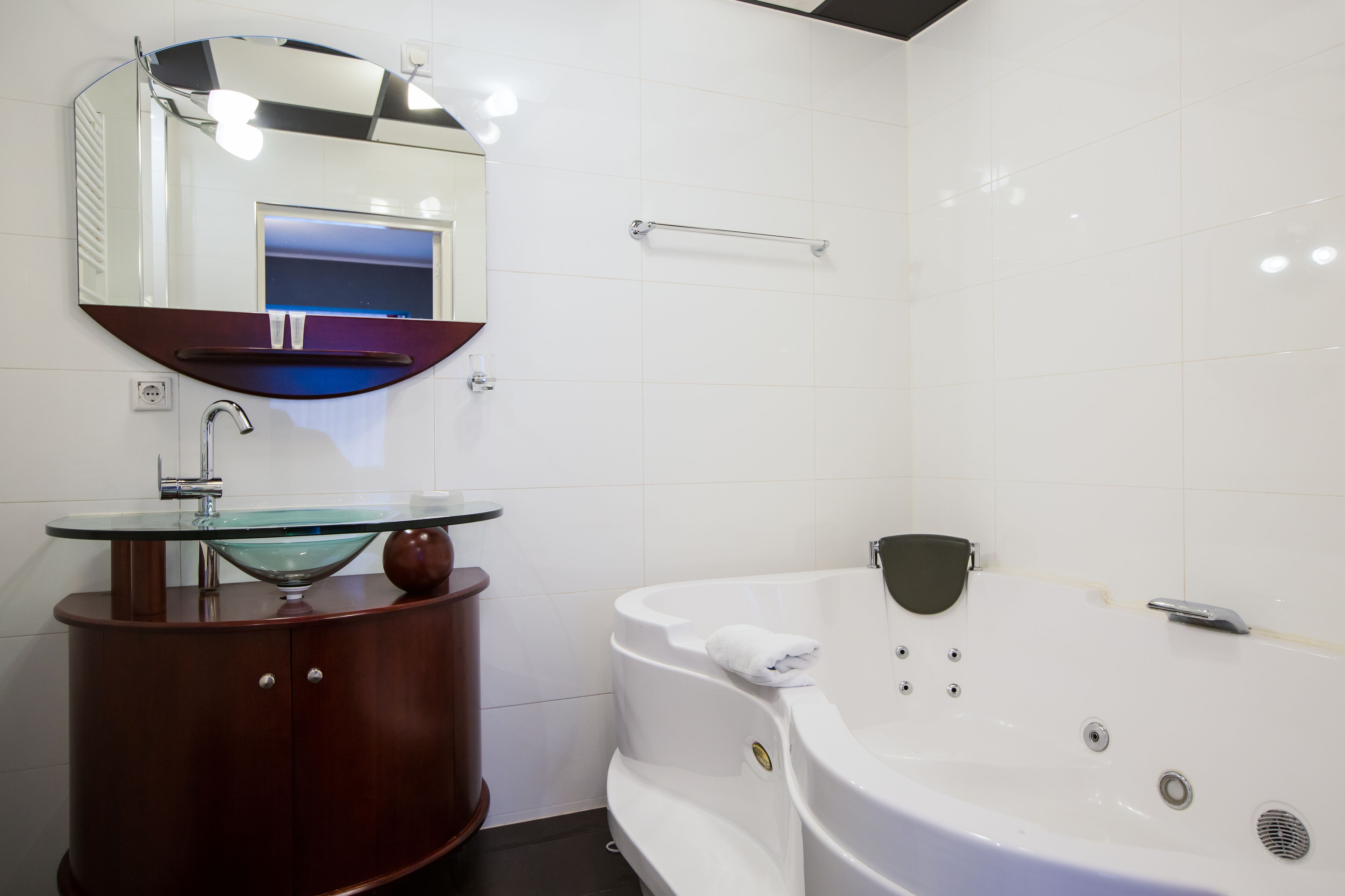 A bathroom with a glass-topped sink, a wooden vanity, a white bathtub, and a large mirror.