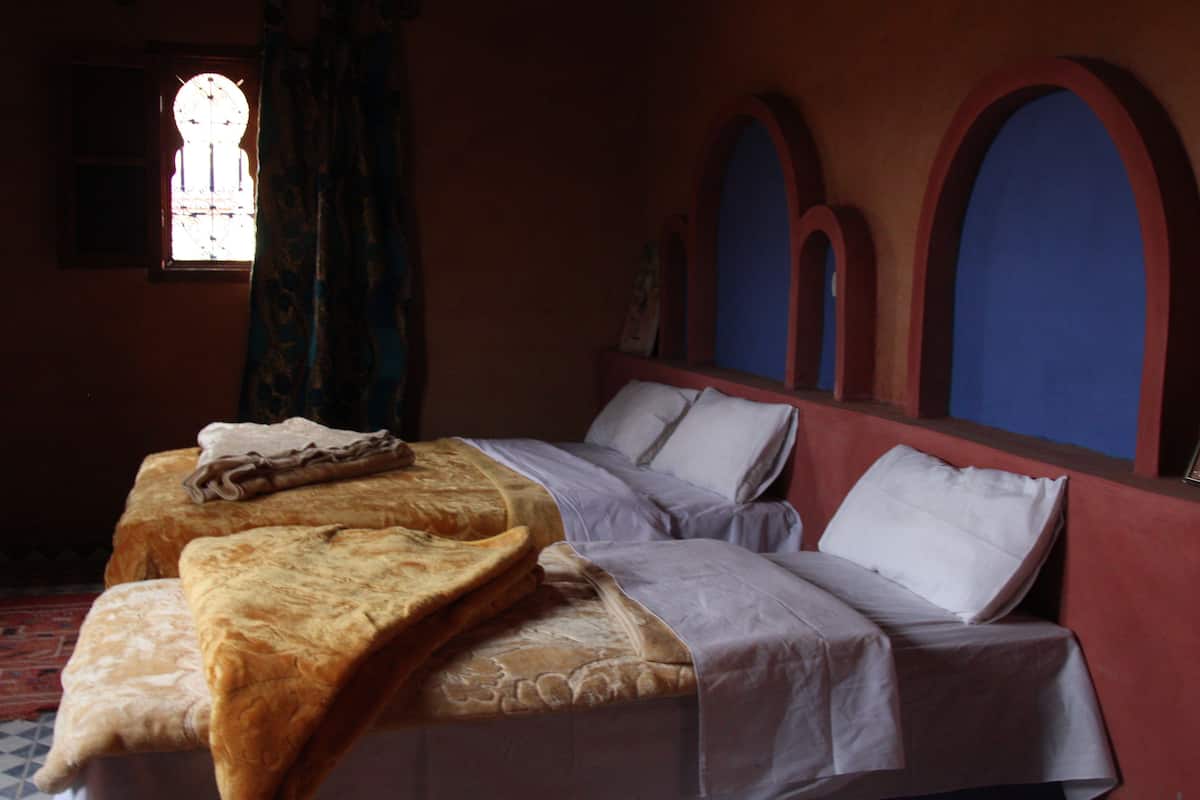 A room with a bed, a window with curtains, and a wall with arches.