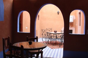 An interior with a round table and chairs, arched doorways, and a tiled floor. - Riad Aicha (Taouz)