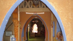 An arched doorway leading into a room with a tiled floor, a framed patent certificate, and a small table with a scale. - Riad Aicha (Taouz)