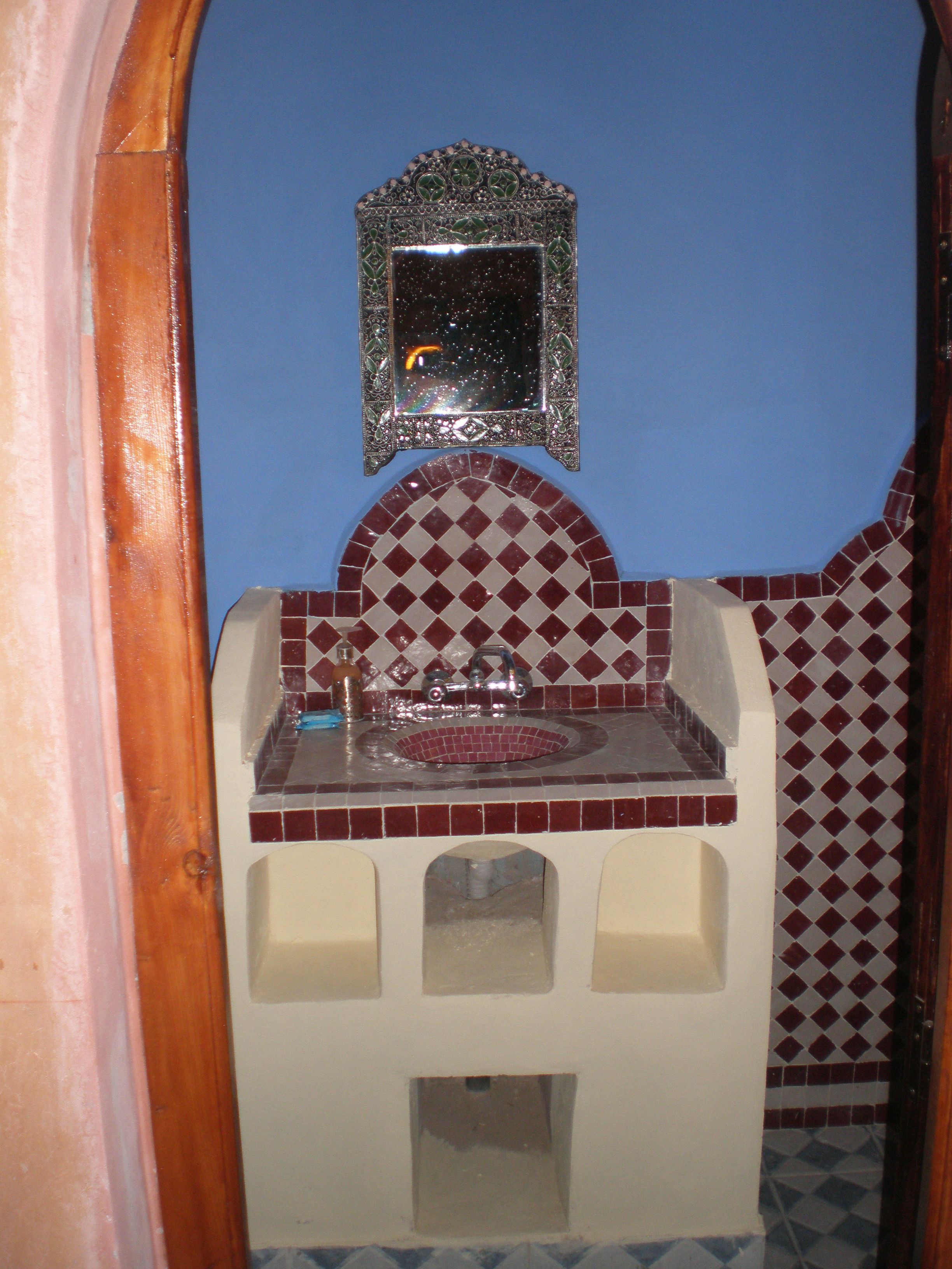 Un baño con lavamanos, espejo y azulejos estampados.