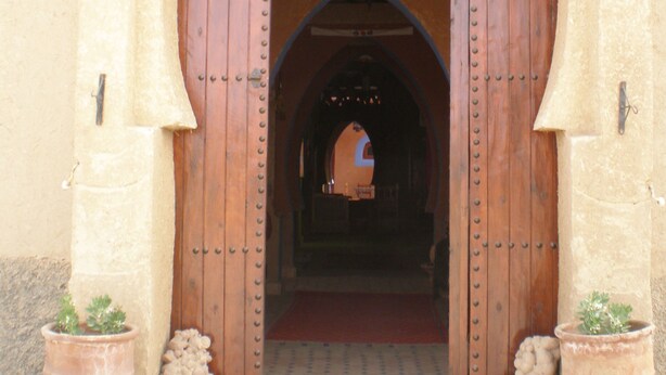 A large wooden door with a pointed arch, flanked by two potted plants. - Riad Aicha (Taouz)