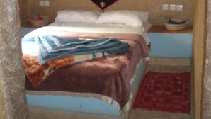A bedroom with a bed, a hanging chair, a small table, and a wall-mounted shelf. - Riad Aicha (Taouz)