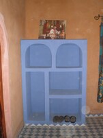 Una habitación con un armario azul con varios estantes, piso de baldosas y un cuadro enmarcado encima.