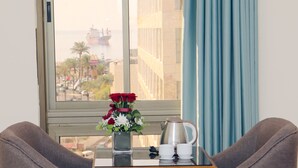 Una habitación con vistas a un paisaje urbano a través de una ventana, una mesa con una cafetera, dos sillas y un florero con flores.