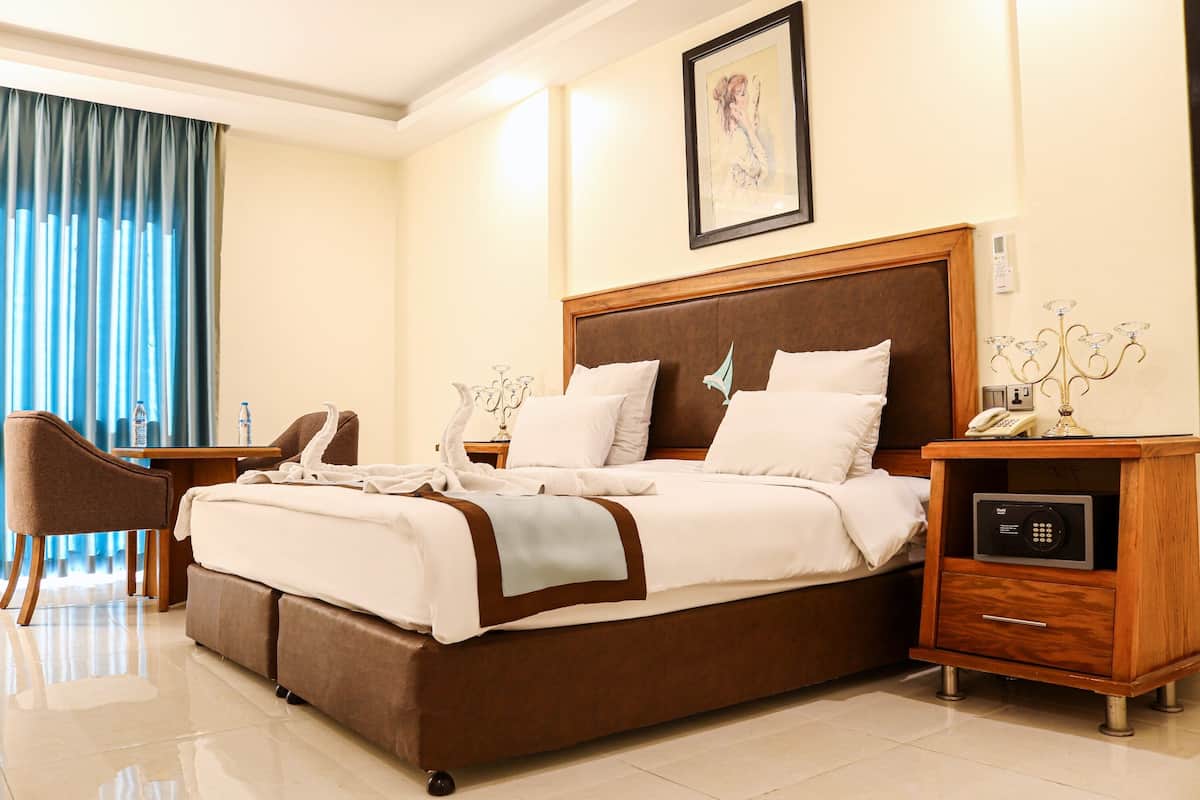 Quarto de hotel com uma cama grande, uma escrivaninha, uma cadeira e uma mesa de cabeceira com telefone e abajur.