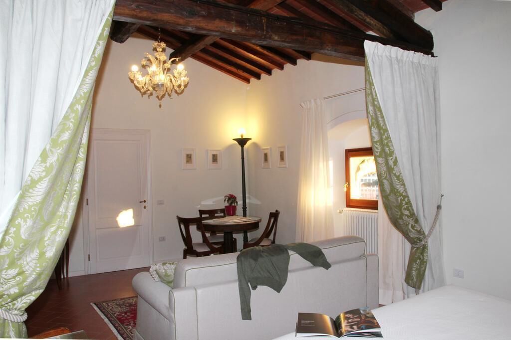 A cozy room with a white sofa, a dining table with chairs, a chandelier, and a window with curtains.
