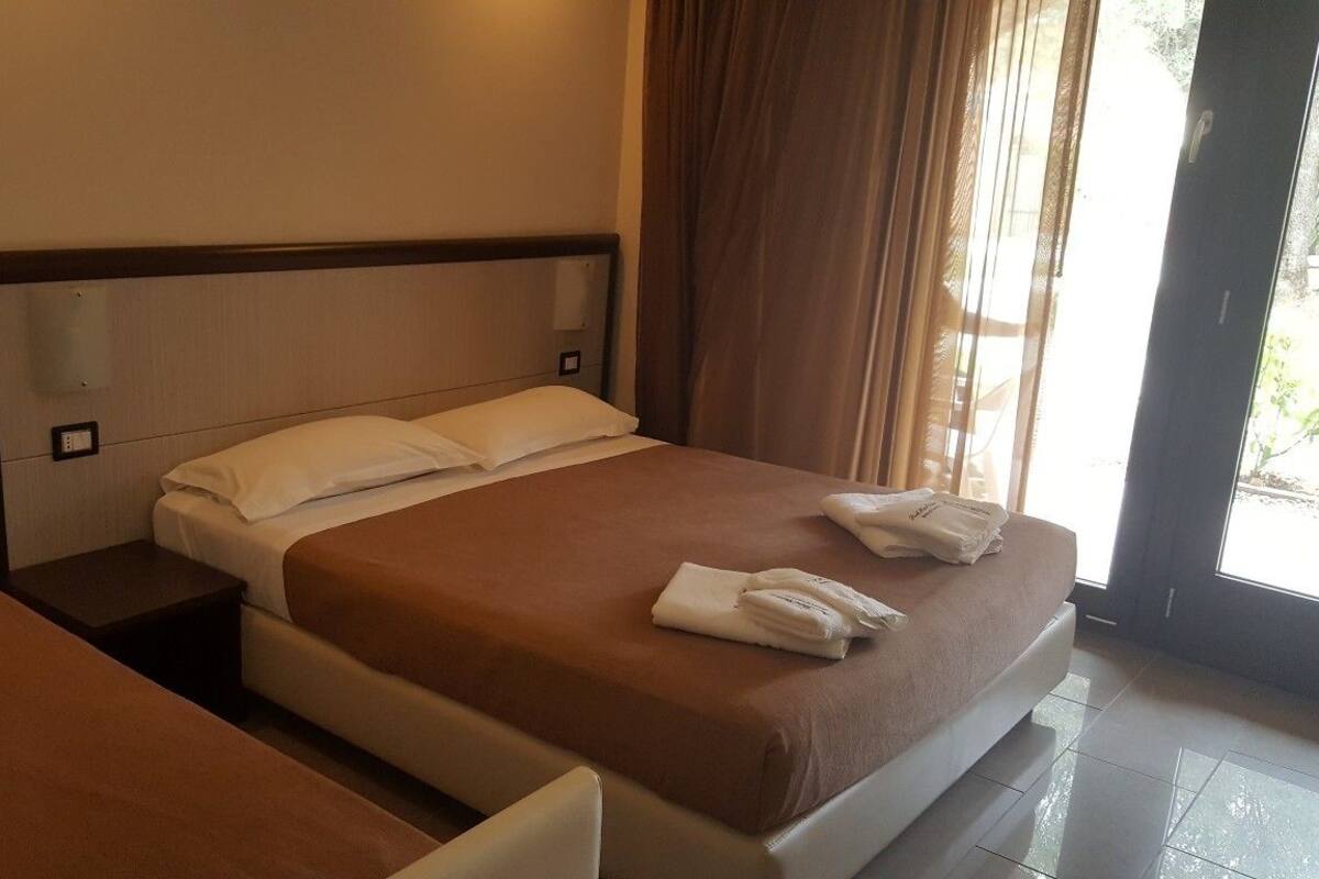 Une chambre d’hôtel avec un lit, une table de chevet, un banc et une fenêtre avec des rideaux.