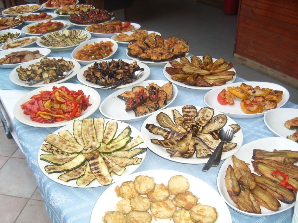 Une table où sont présentés divers plats, notamment des légumes et de la viande grillés.