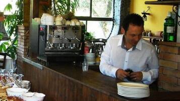 A bar area with a coffee machine, shelves with bottles, and a table with food and plates.