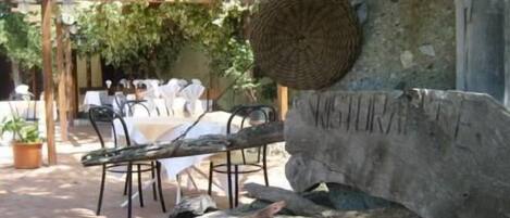 An outdoor dining area with a rustic stone wall, wooden pergola, and tables set for dining.