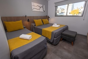 A hotel room with two beds, a small sofa, a window with a view, and a wall-mounted artwork. - Hotel King'S Bariloche (San Carlos de Bariloche)