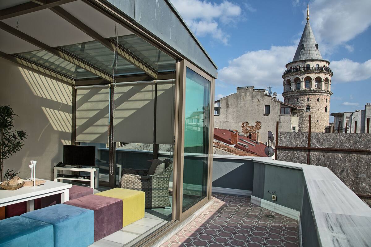 A modern balcony with a glass enclosure, a sofa, a TV, and a dining table.