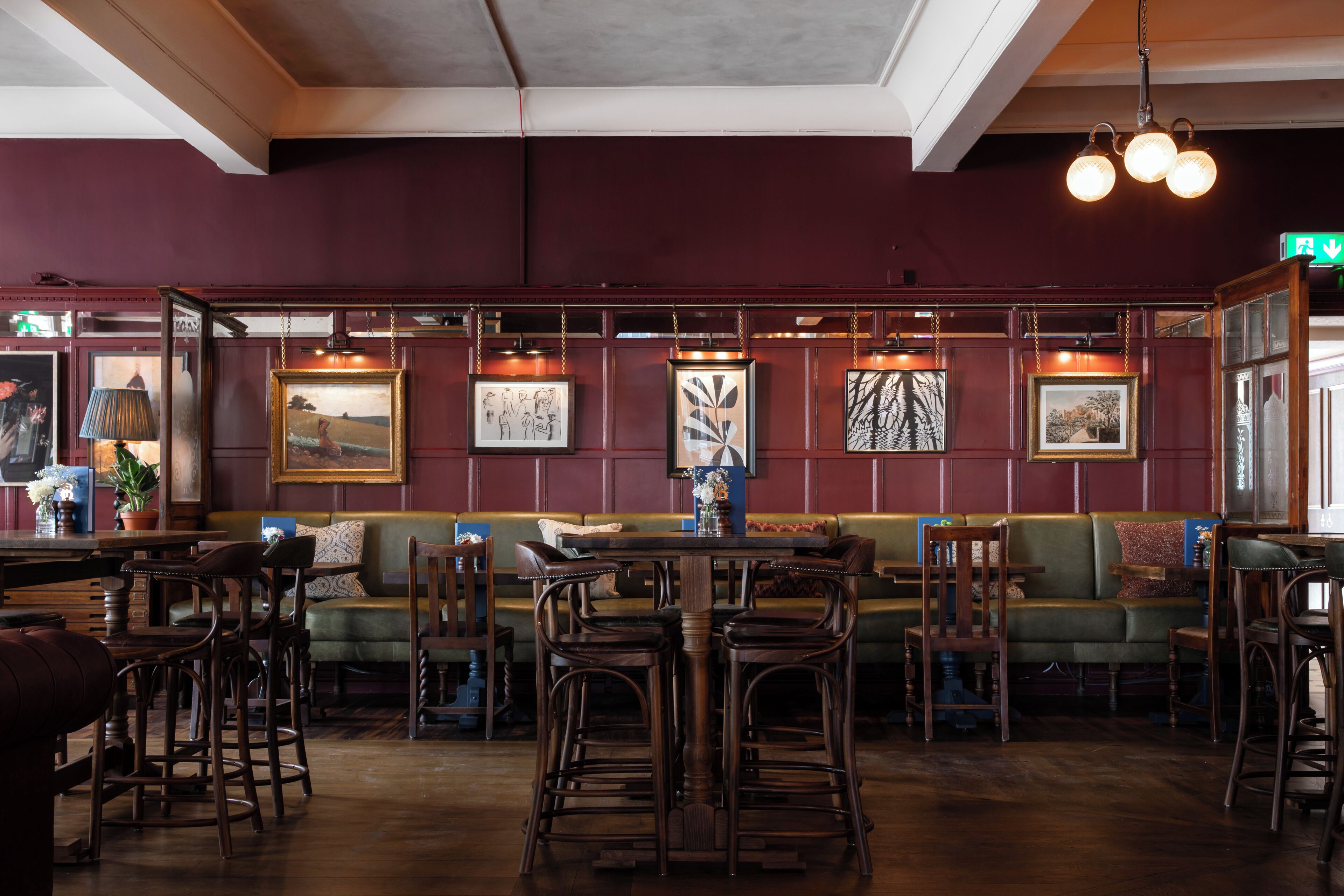 A restaurant interior with wooden furniture, a green booth, and framed artwork on the walls.