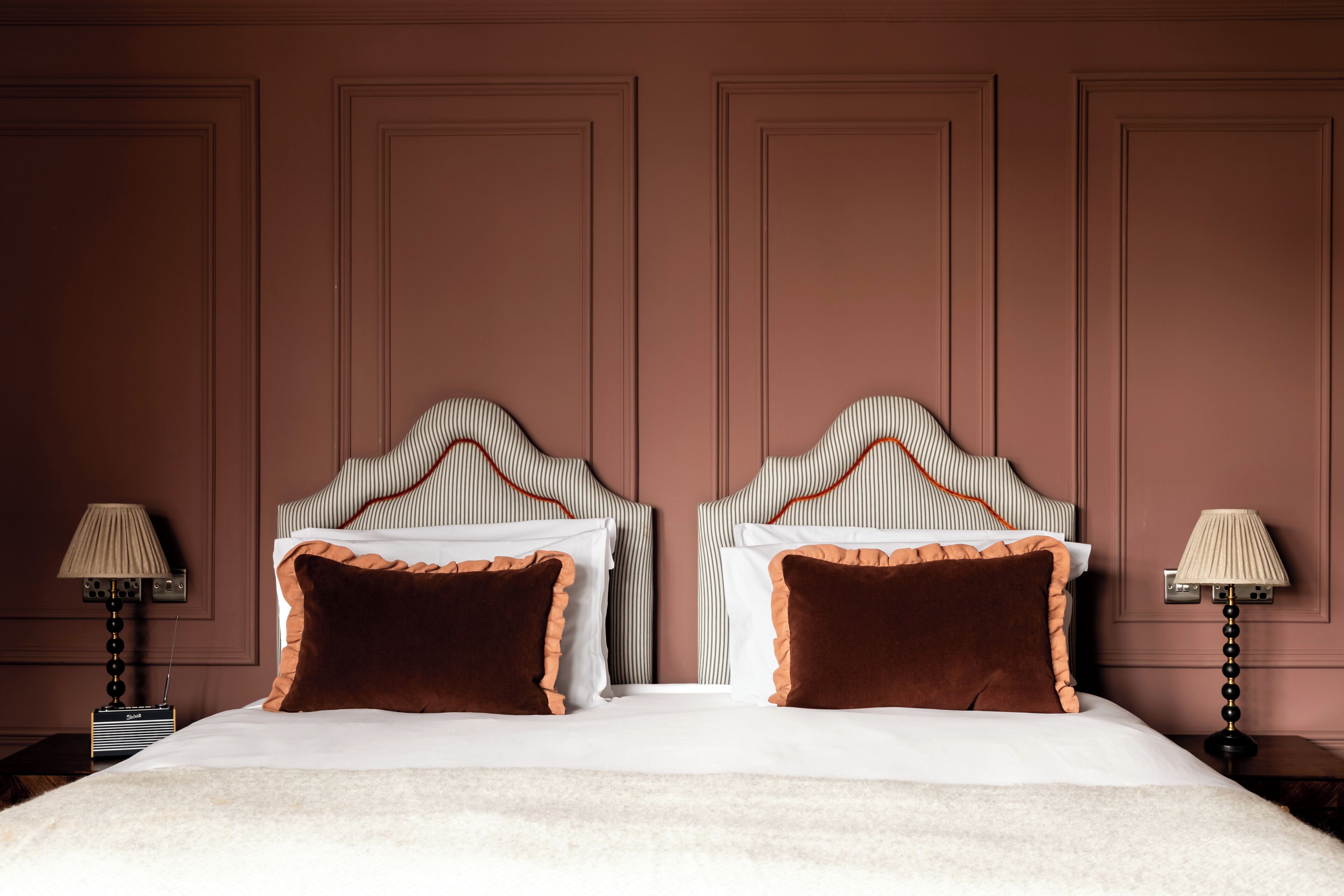 A double bed with a white and brown color scheme, flanked by two nightstands with lamps.