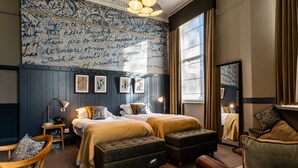 A hotel room with a large bed, two bedside tables, a desk, and a chair. There are framed pictures on the wall and a window with curtains. - Brook Green Hotel (London)