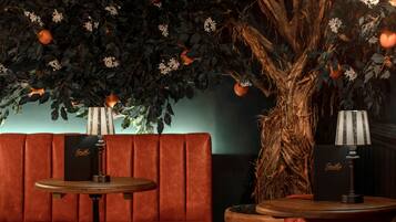 A cozy seating area with a sofa and two small tables, each with a lamp. A large tree with oranges and white flowers is in the background.