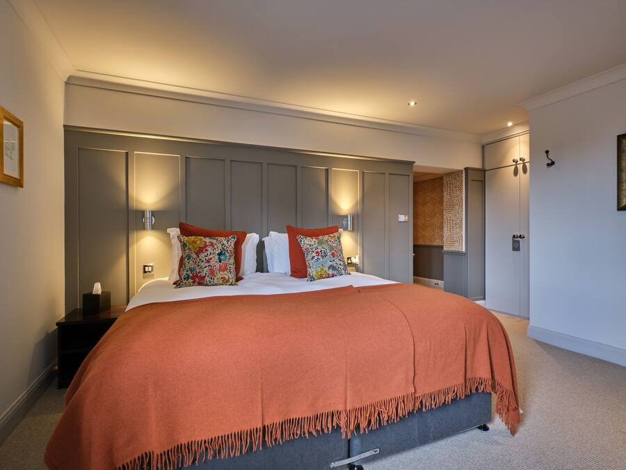 A bedroom with a large bed, a nightstand, a wardrobe, and a wall-mounted lamp.