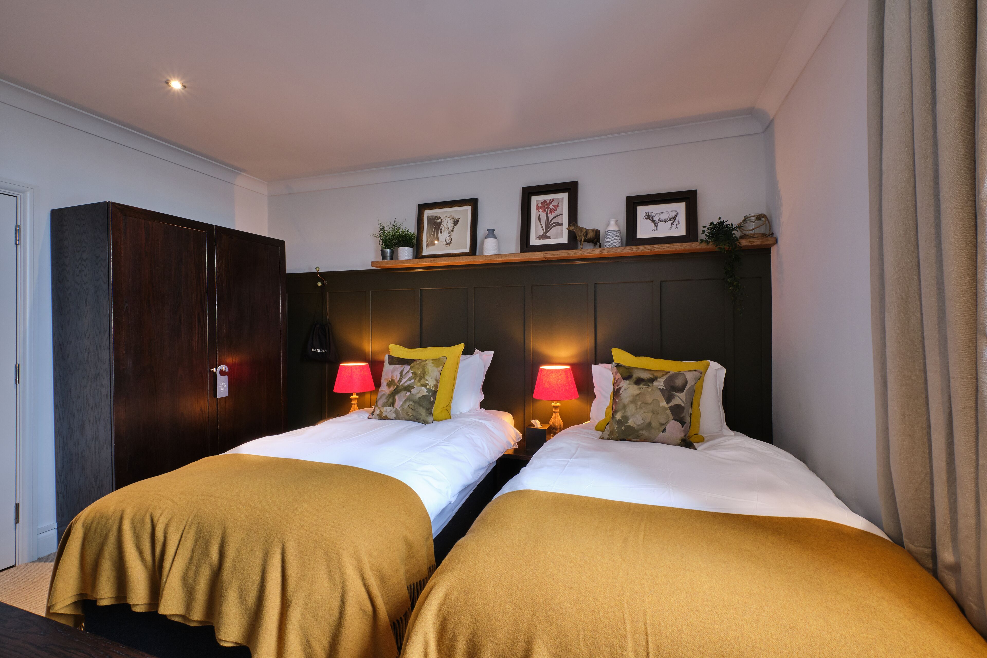 Une chambre d’hôtel avec deux lits, chacun recouvert d’une couverture marron, une armoire en bois, une étagère avec des photos encadrées et des lampes de chevet.