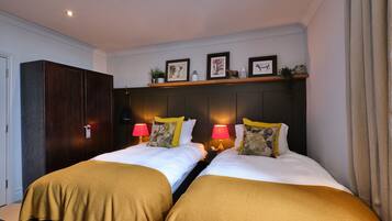 Une chambre d’hôtel avec deux lits, chacun recouvert d’une couverture marron, une armoire en bois, une étagère avec des photos encadrées et des lampes de chevet.