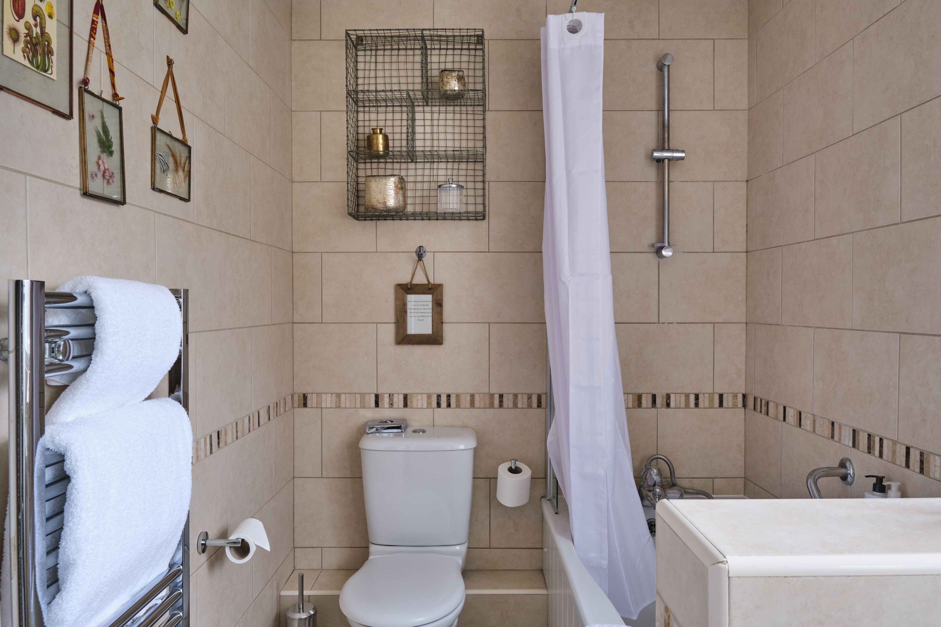 A bathroom with a toilet, shower, and bathtub. There are towels hanging on a rack, a framed picture on the wall, and a shelf with decorative items.