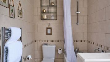 A bathroom with a toilet, shower, and bathtub. There are towels hanging on a rack, a framed picture on the wall, and a shelf with decorative items.