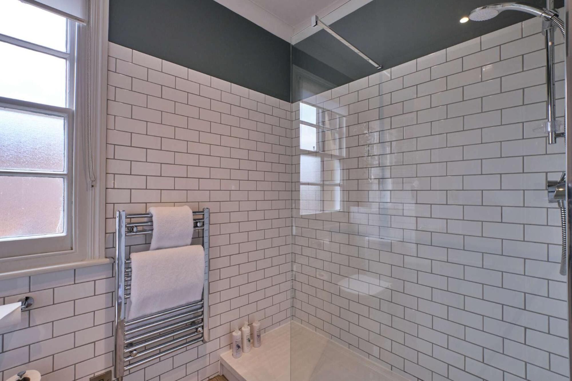 A modern bathroom with white subway tiles, a glass shower enclosure, and a towel rack with a white towel.