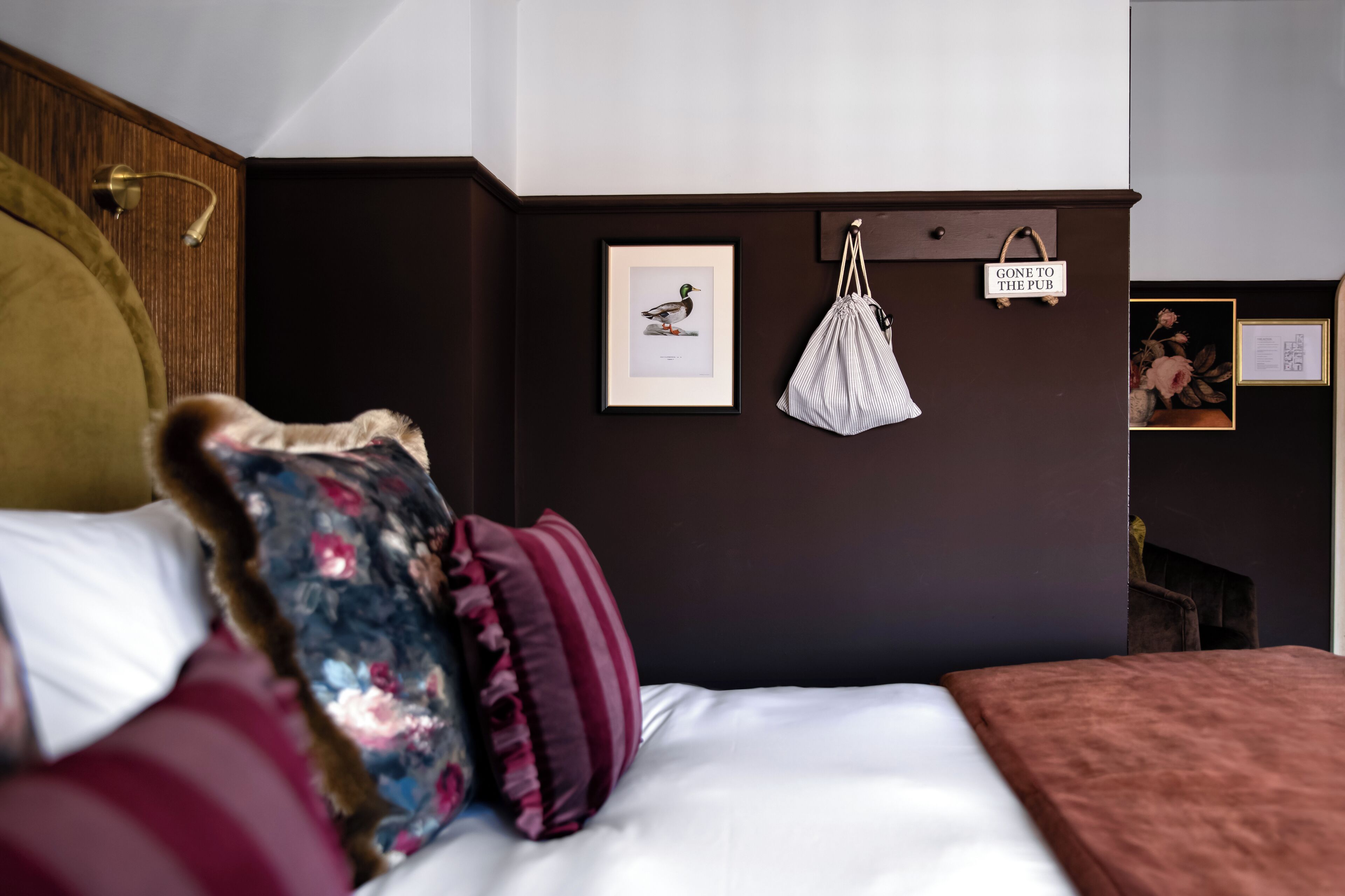 Un dormitorio con cama, almohadas, un bolso colgado y cuadros en la pared.
