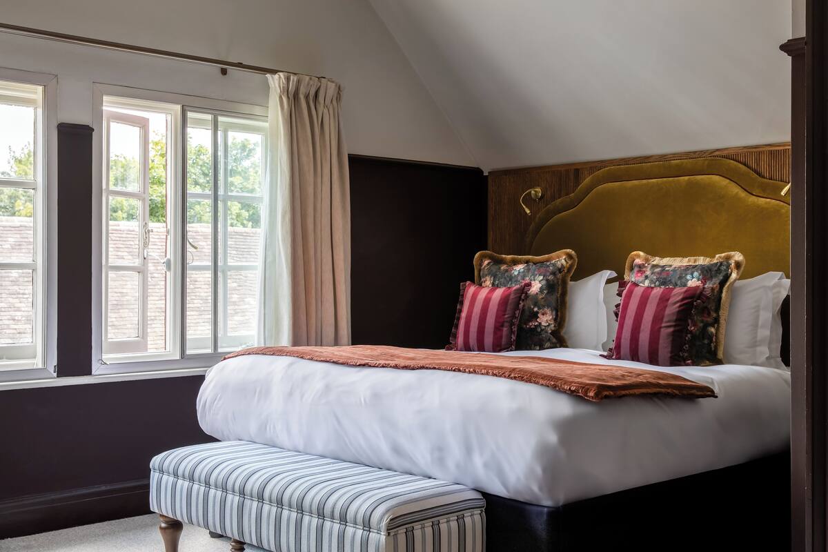 A bedroom with a large bed, a bench, and a window with curtains.