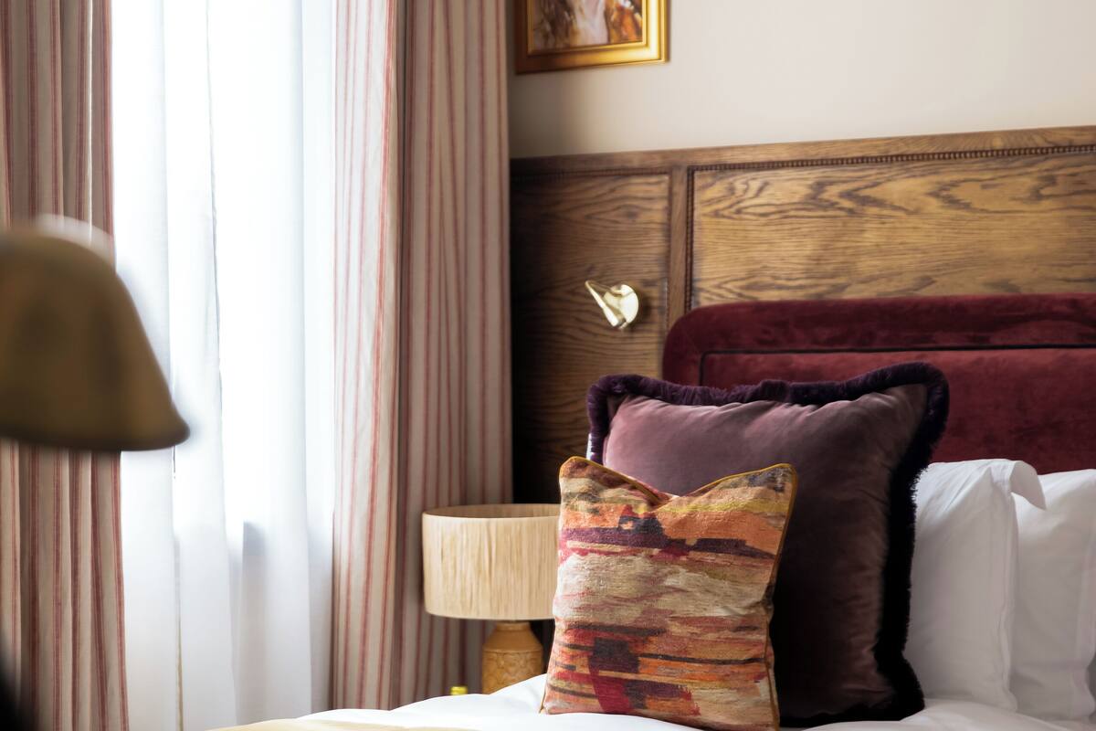 A hotel room with a large bed, a wooden headboard, a nightstand with a lamp, and a painting on the wall.