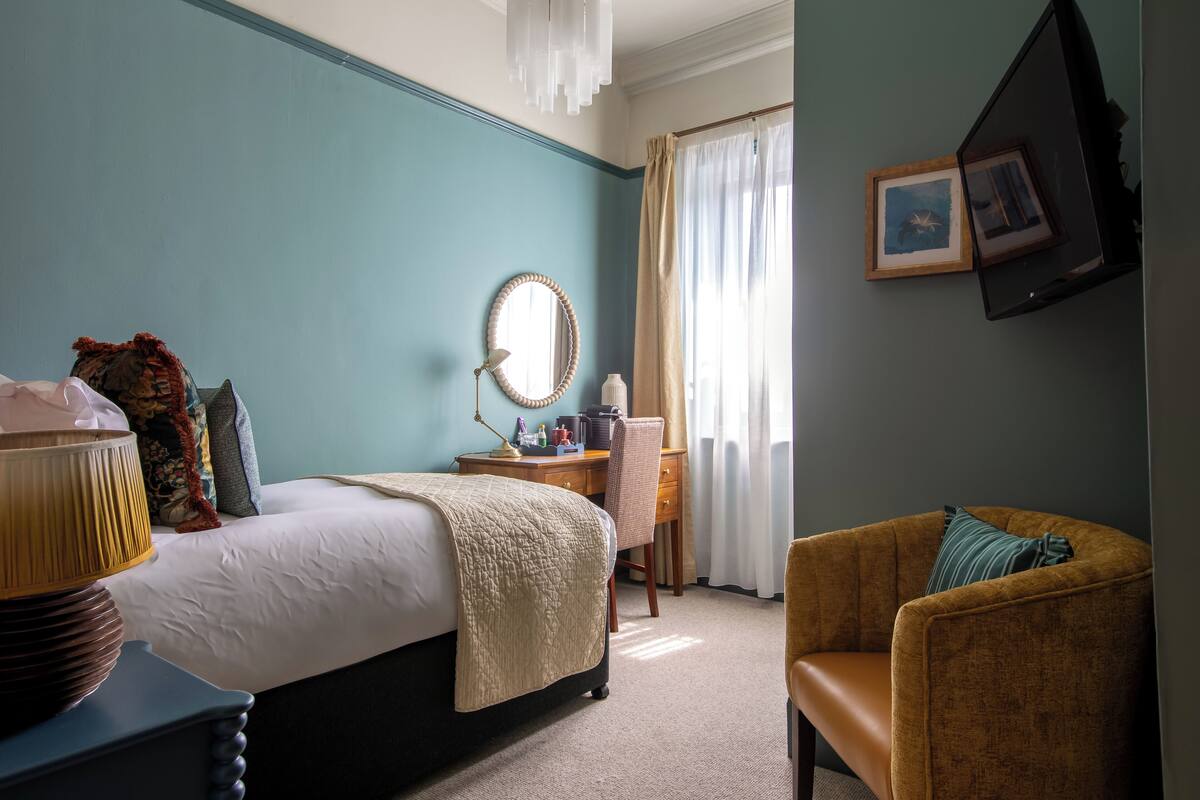 A hotel room with a bed, a desk, a chair, a lamp, and a window with curtains.