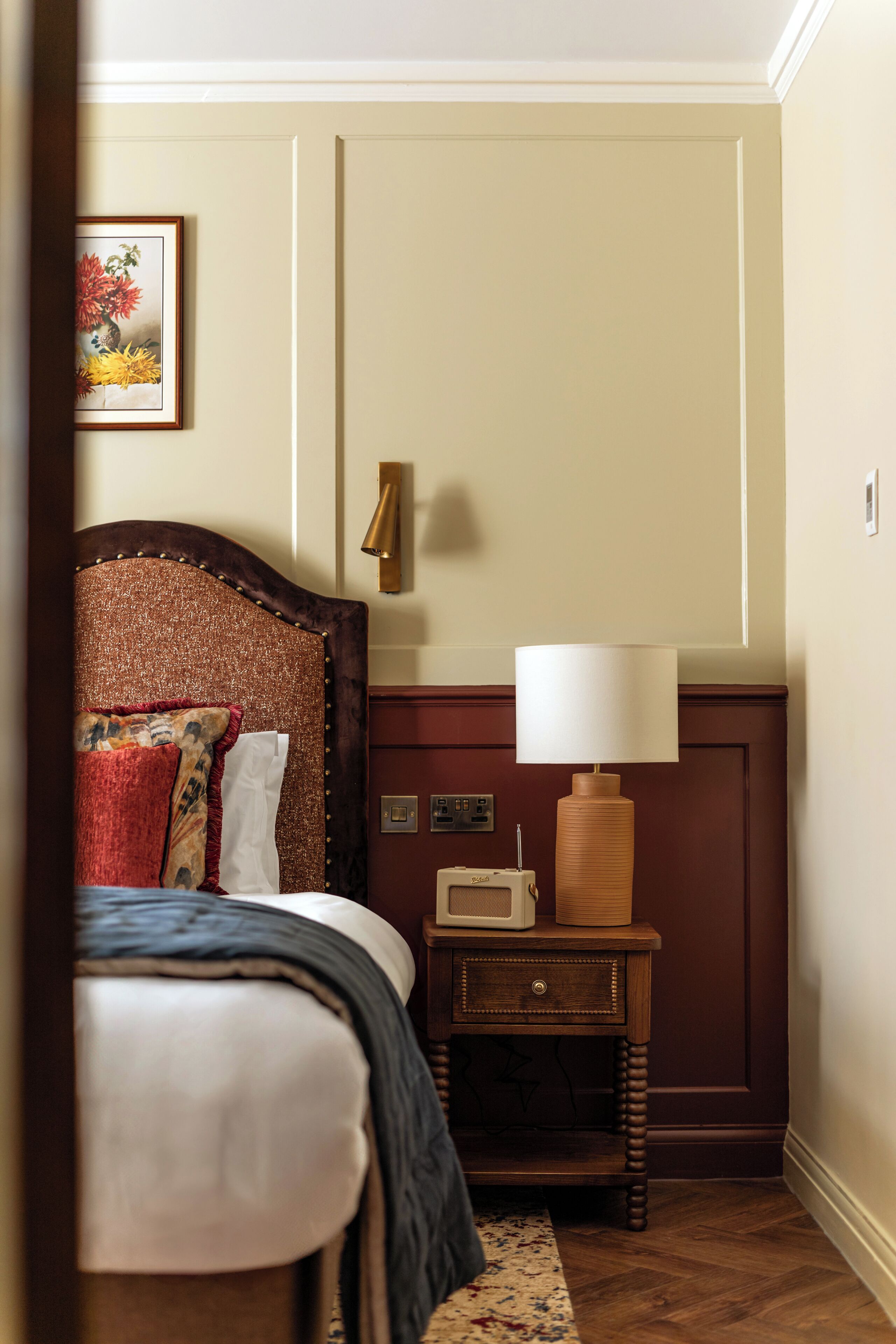 Ein Hotelzimmer mit Bett, Nachttisch mit Lampe und einem gerahmten Bild an der Wand.