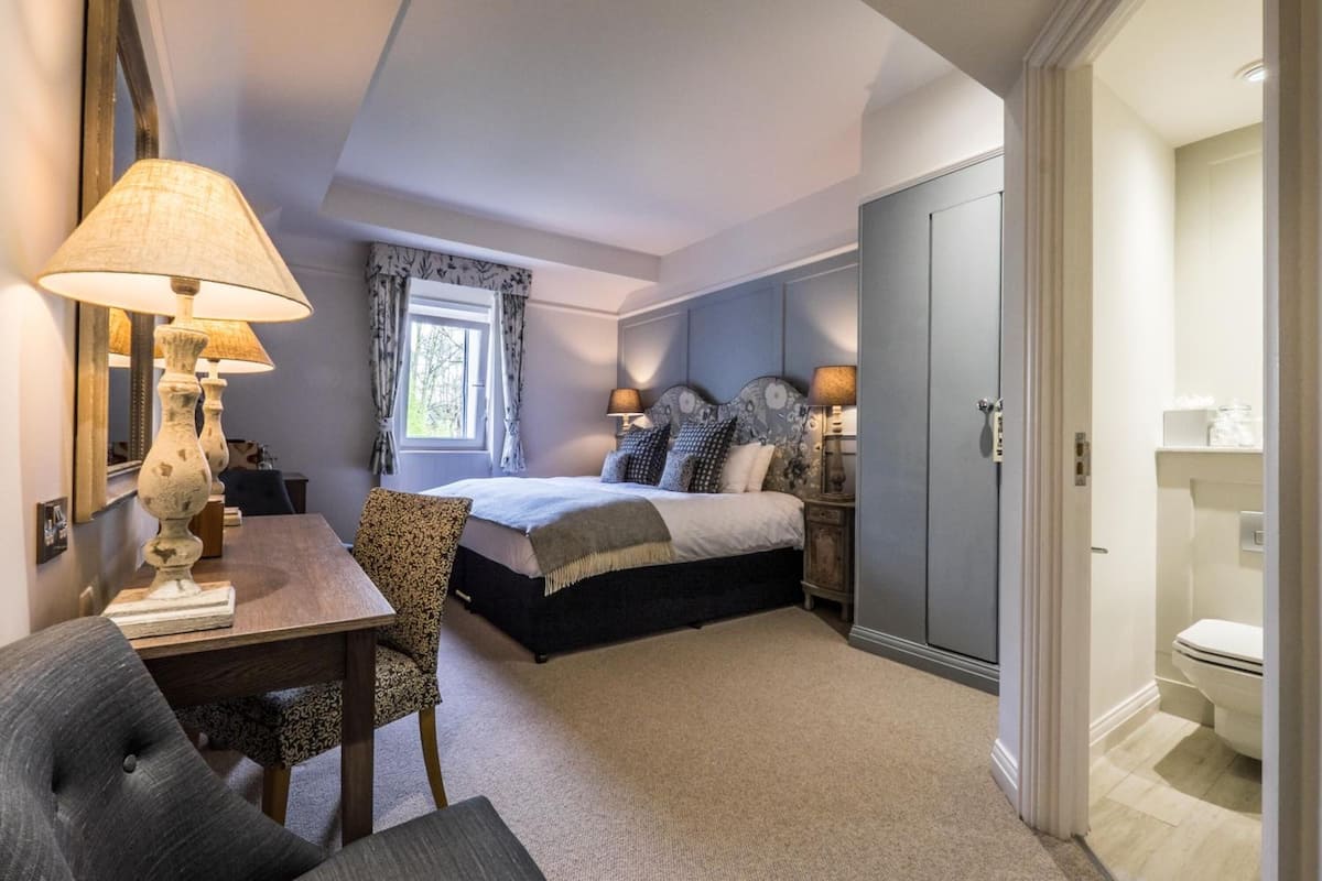 A bedroom with a bed, bedside tables, a desk, a chair, a lamp, and a wardrobe.