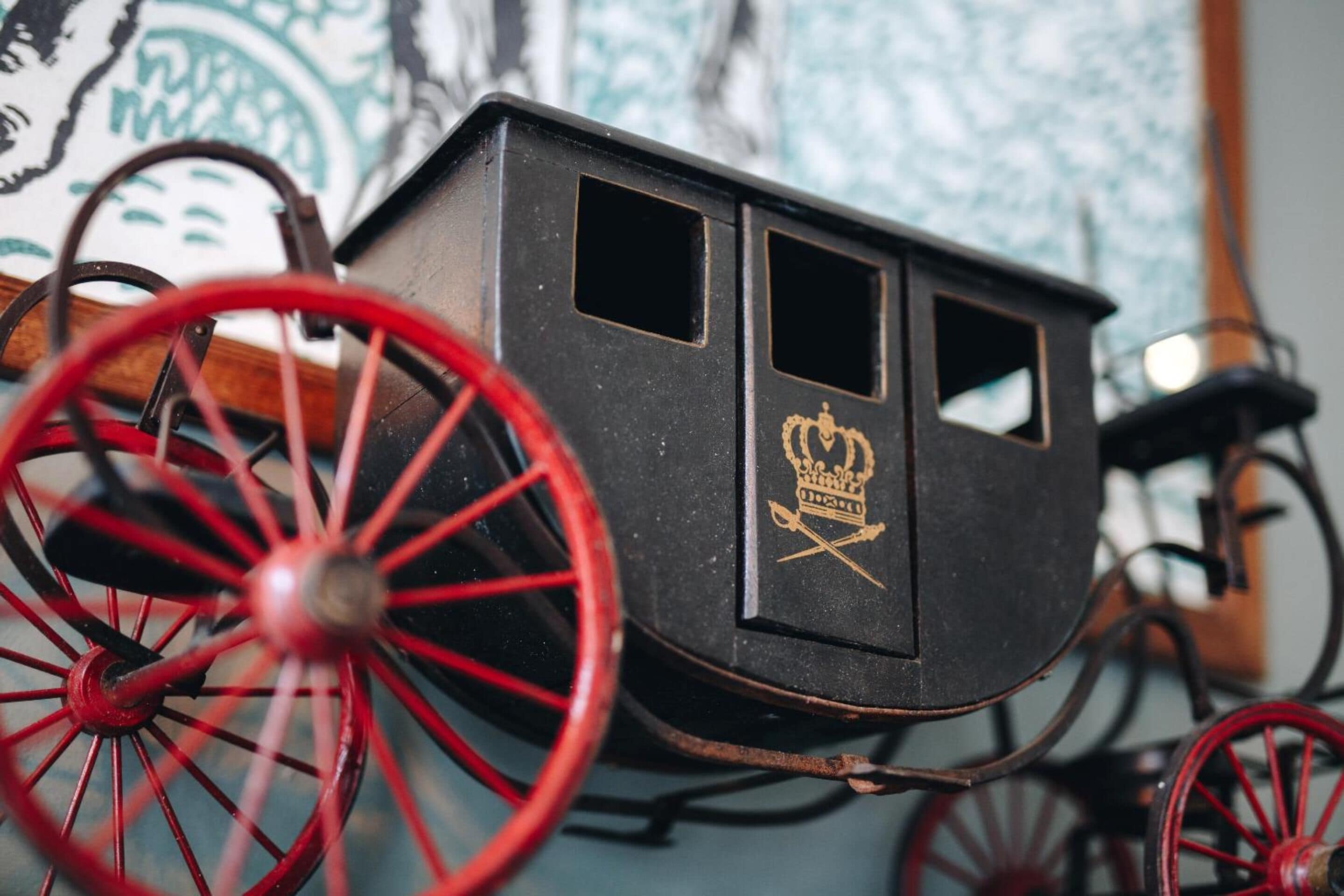 Ein historischer Wagen mit roten Rädern und dunkelroter Karosserie, mit einem goldenen Wappen an der Seite.