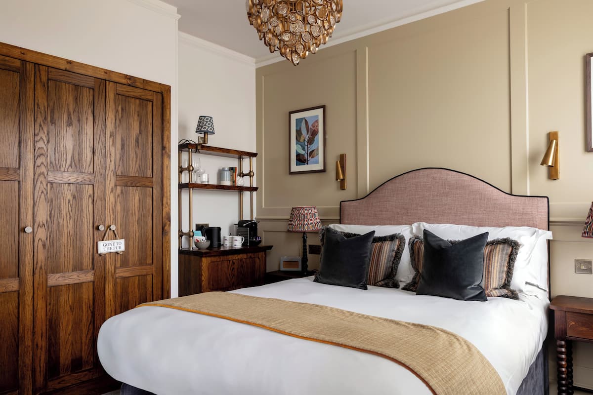 A hotel room with a large bed, wooden wardrobe, bedside table with lamp, and a framed picture on the wall.