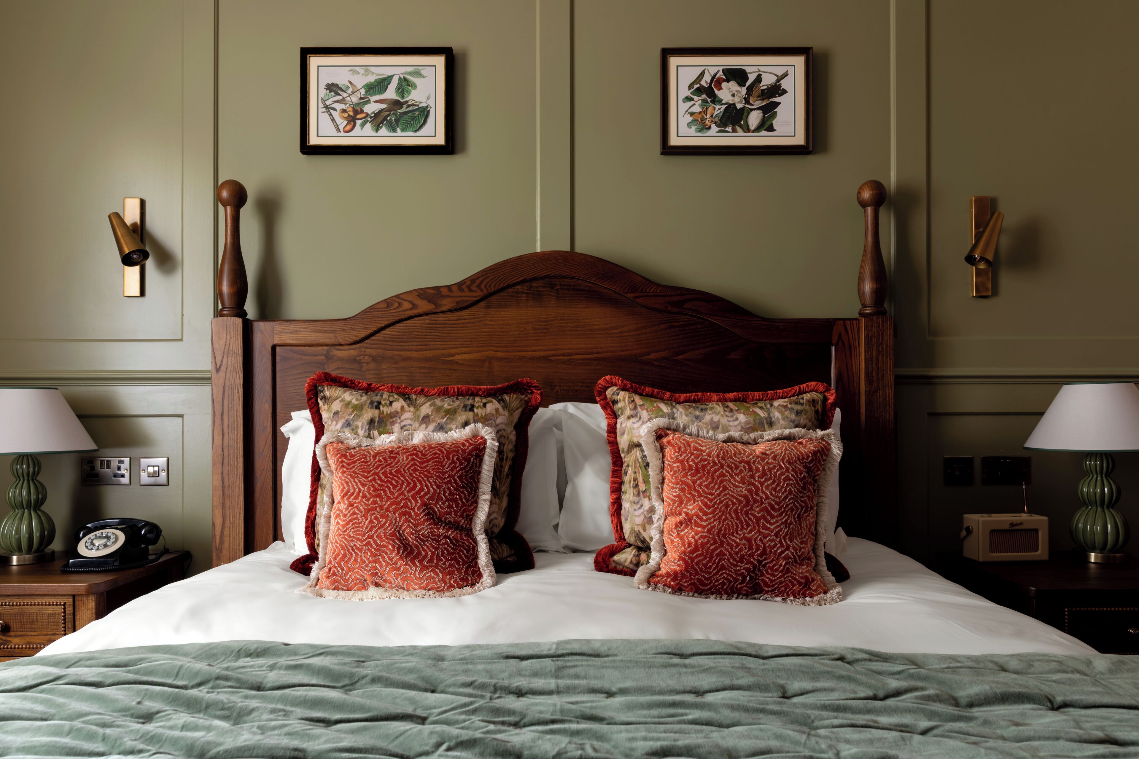 Un lit bien fait, avec une tête de lit en bois, deux oreillers assortis et une couverture verte. Deux tableaux encadrés sont accrochés au mur, au-dessus du lit.