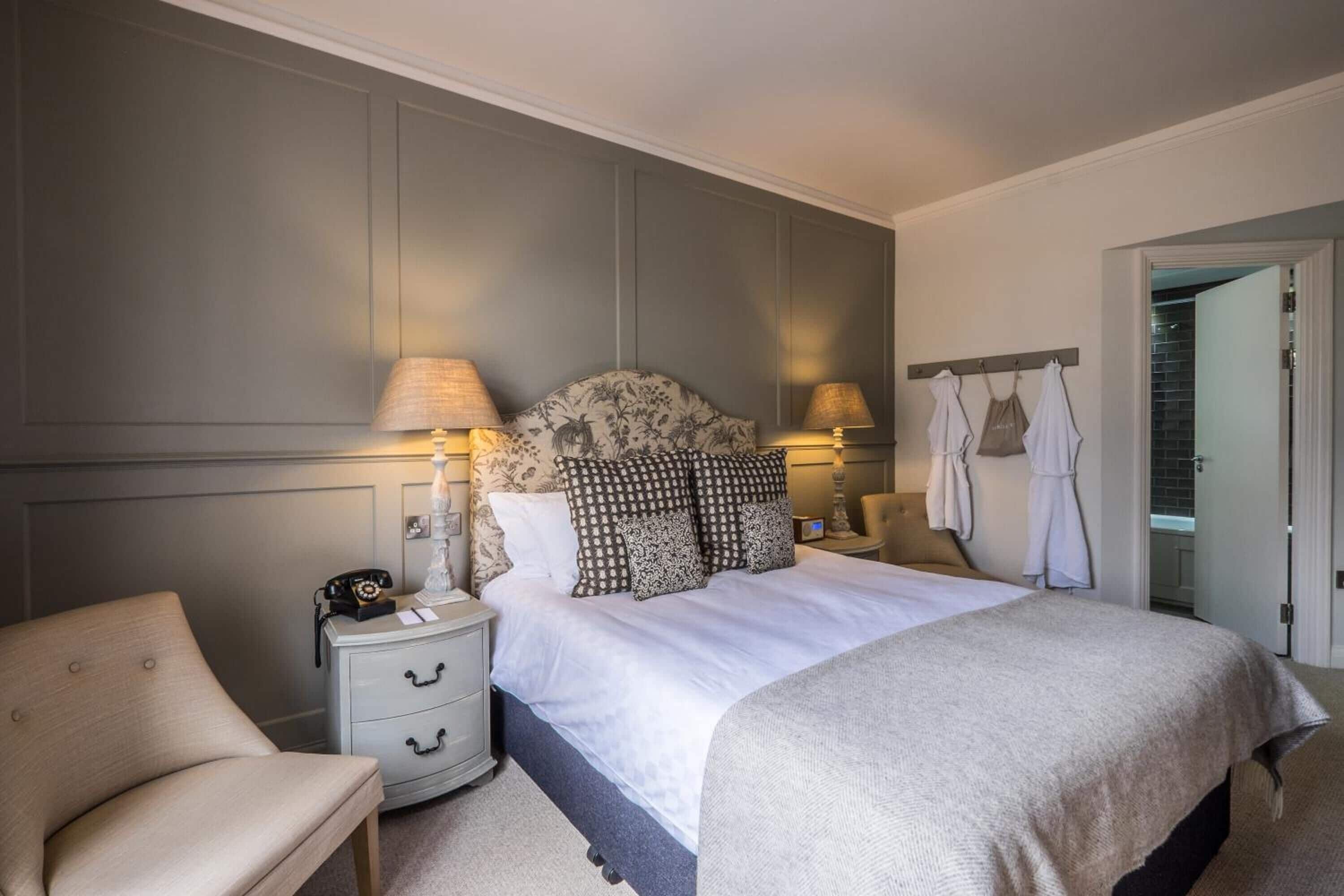 A neatly arranged bedroom with a large bed, bedside lamps, a nightstand, and a chair.