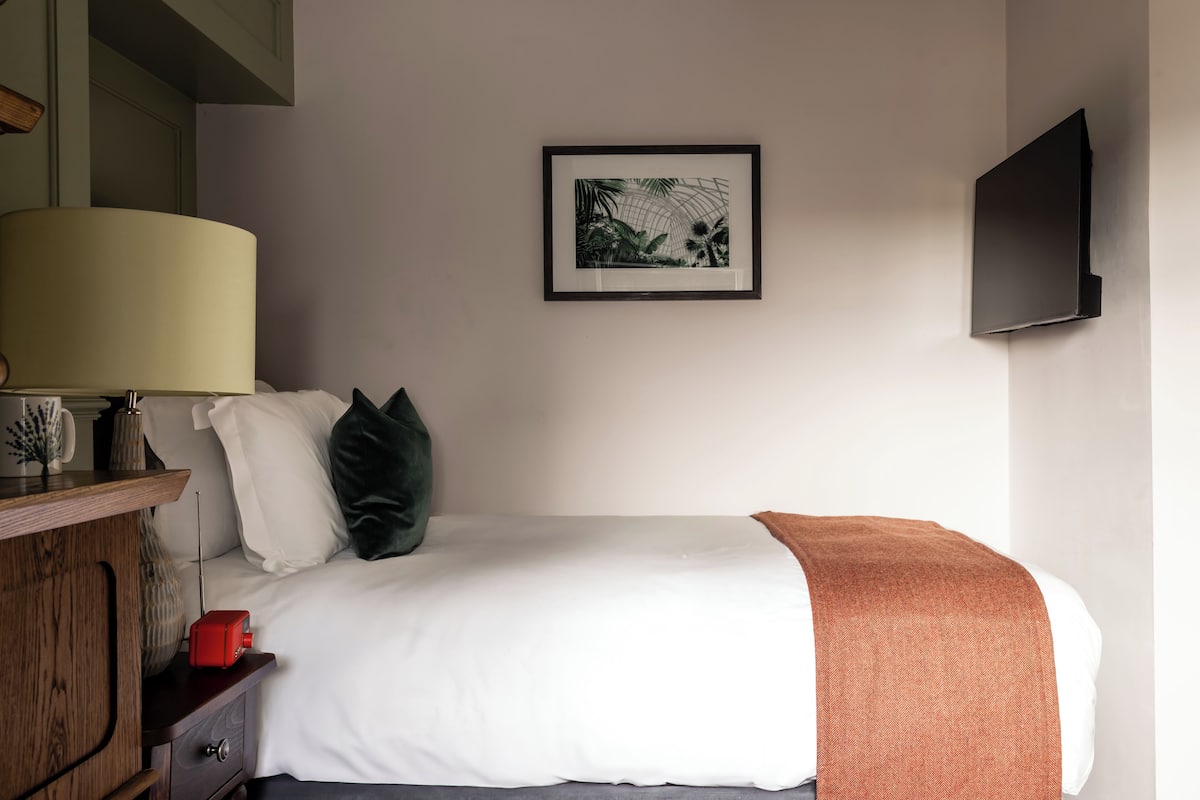 A neatly made bed with white bedding, a brown throw blanket, and a framed picture above it.