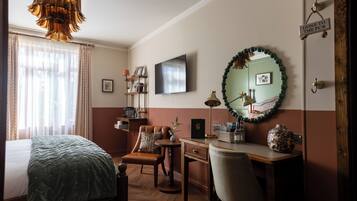 A hotel room with a bed, a desk, a chair, a television, and a mirror.