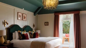 A bedroom with a large bed, a chandelier, a view of the outdoors, and a small table with a chair.