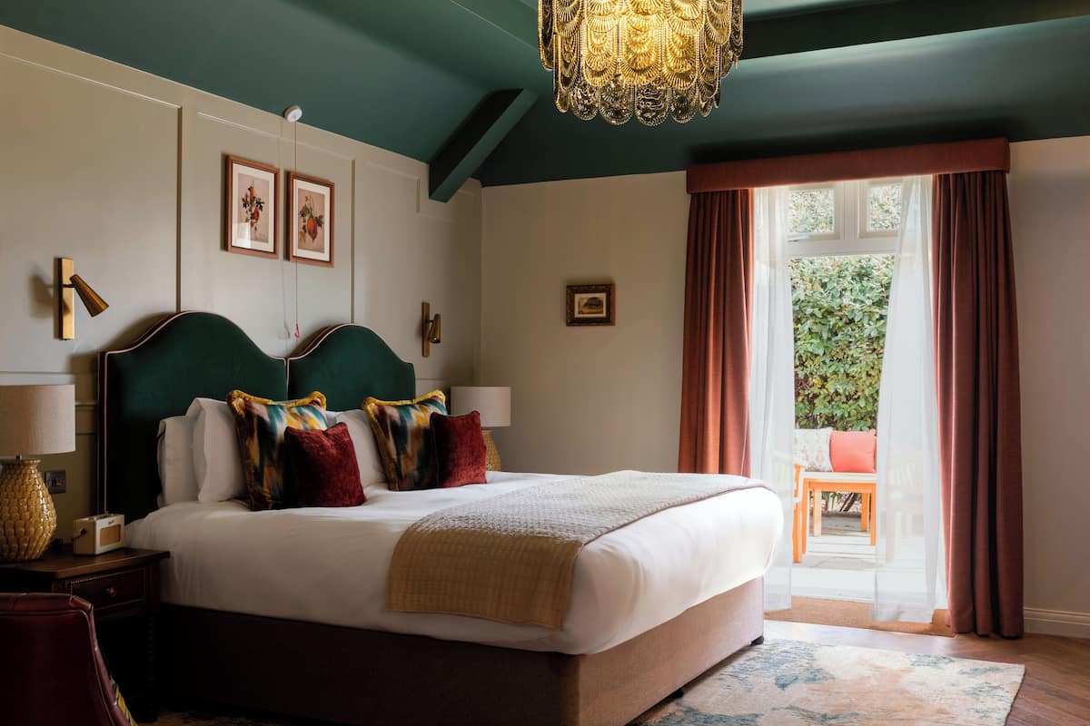 A bedroom with a large bed, a chandelier, a view of the outdoors, and a small table with a chair.
